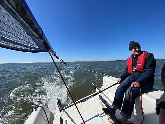 Altbürger und Fördervereinsvorsitzender Axel Hoppenhaus mit Mütze und Rettungsweste am Ruder einer Beneteau First 18.